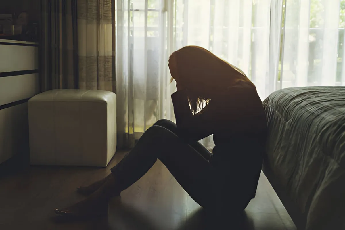 woman sitting on floor next to bed, holding head in anxious and depressed state woman sitting on floor next to bed, holding head in anxious and depressed state