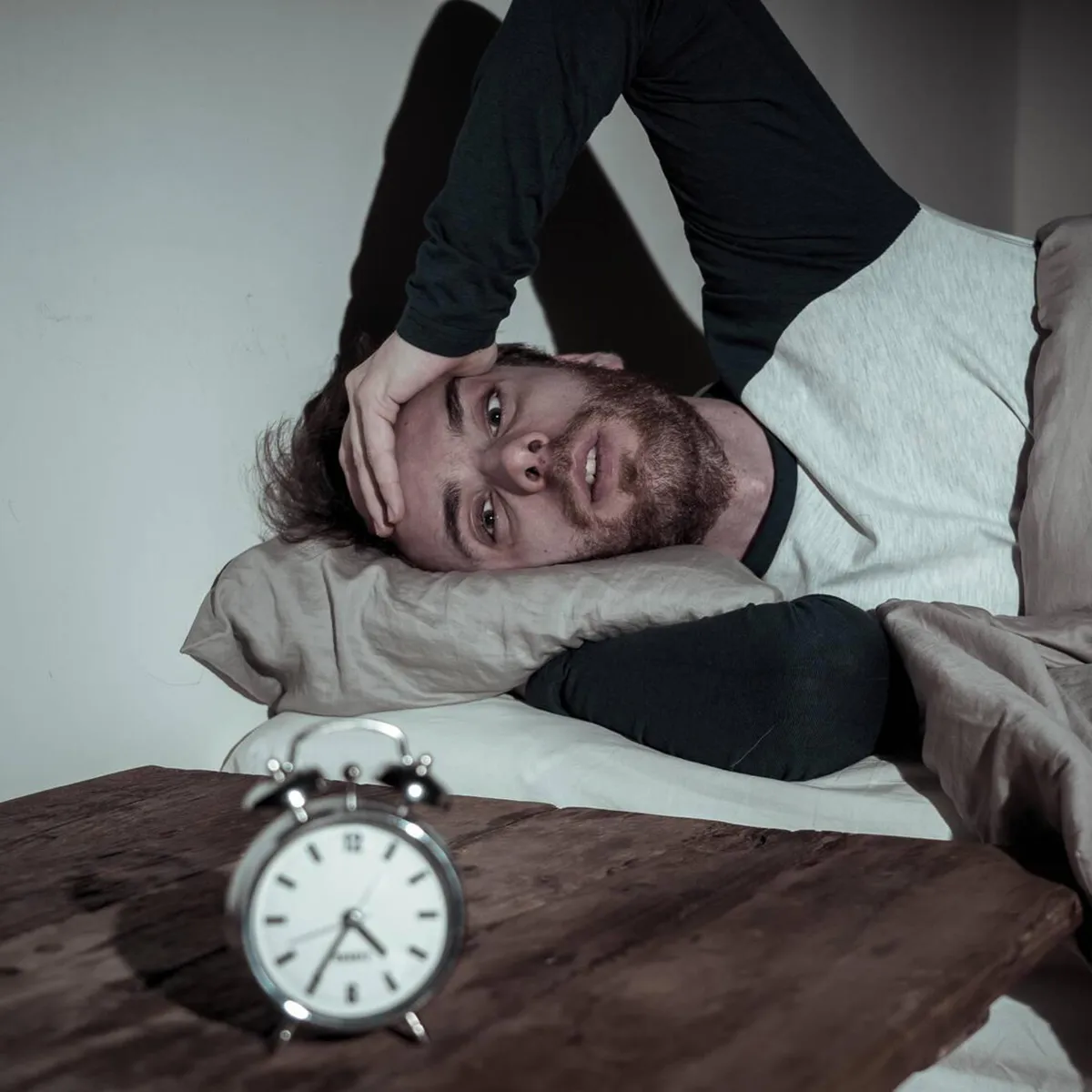 man lying awake in bed, unable to sleep, depicting insomnia as a side effect of taking adderall man lying awake in bed, unable to sleep, depicting insomnia as a side effect of taking adderall